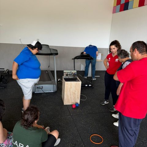 Grupo de pessoas numa sala de ginásio com passadeiras de corrida e material de exercício no chão.