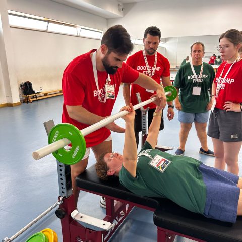 Participantes do Bootcamp 2026 acompanham uma sessão prática de parapowerlifting, onde um formador orienta a execução do exercício de supino adaptado.